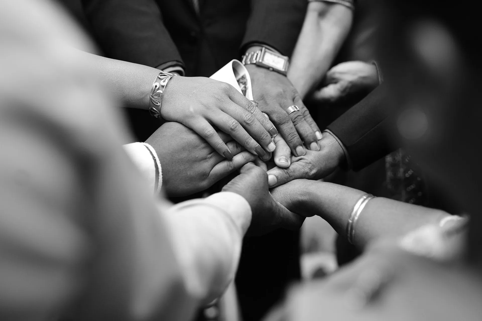 Many hands of different ages and skin tones clasped together in black and white