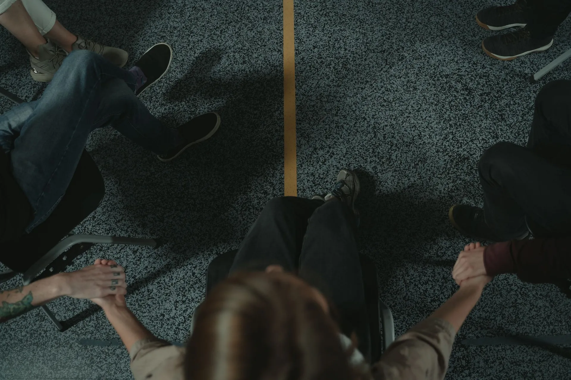Seen from above, a circle of people seated in chairs holding hands