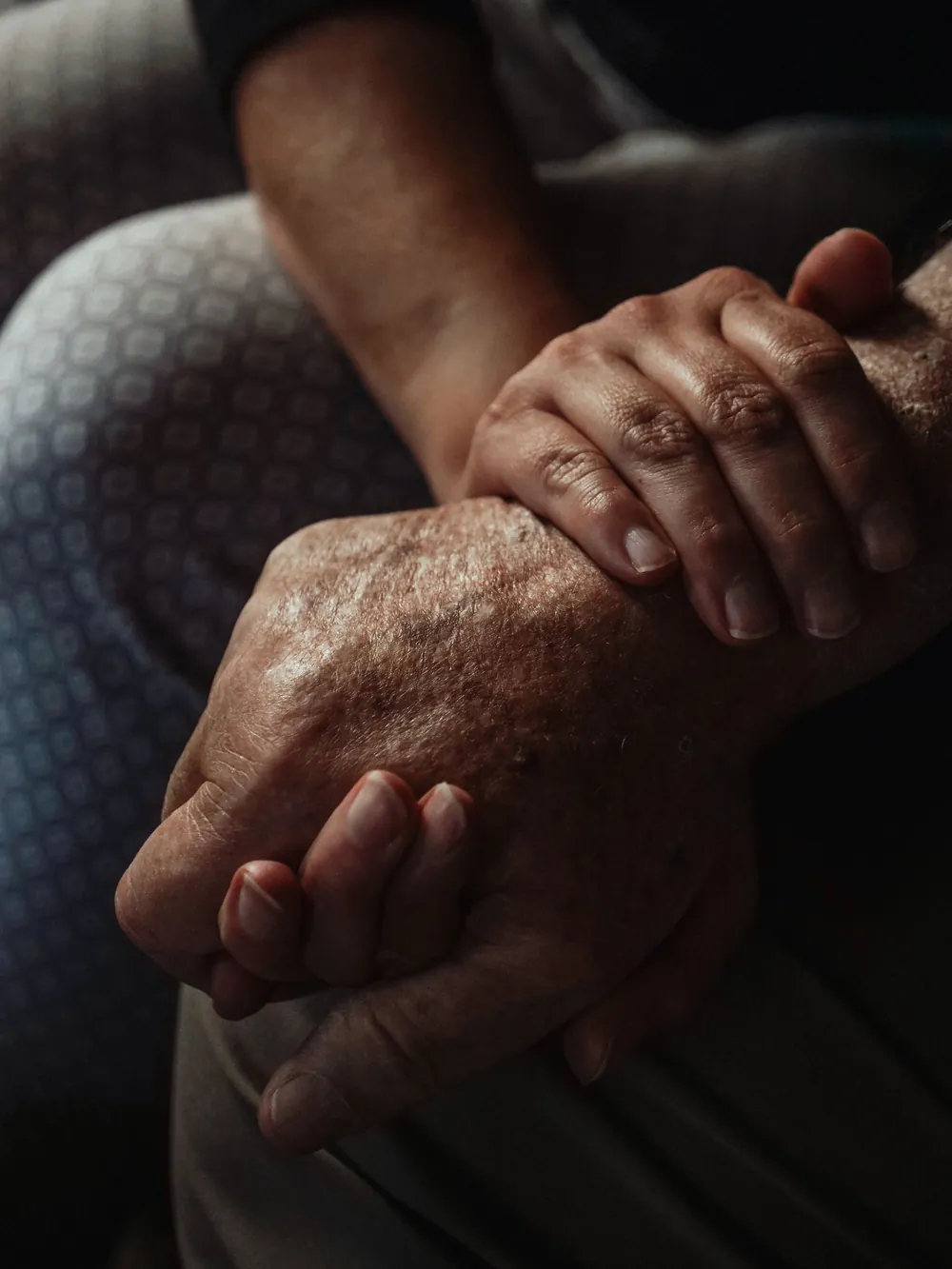 An older hand held gently between a younger person's hands