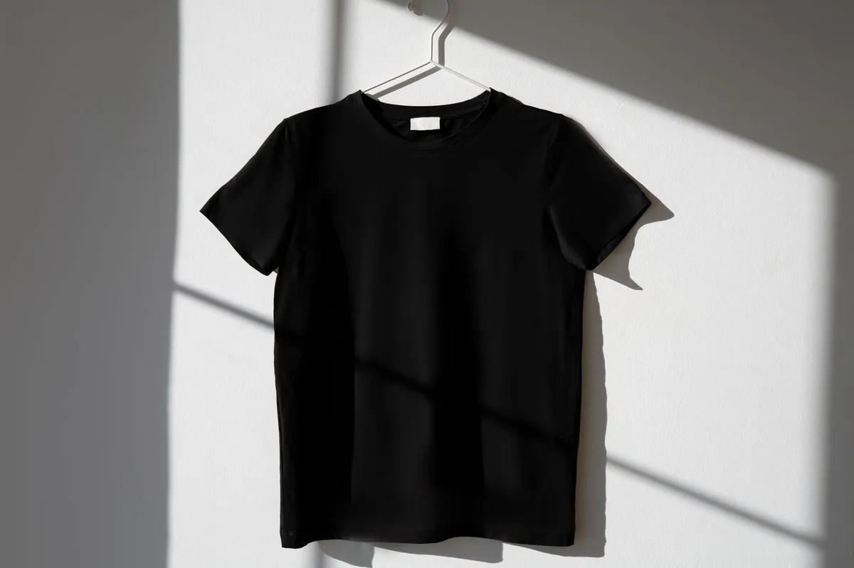 A black t-shirt on a wire hanger against a sunlit wall