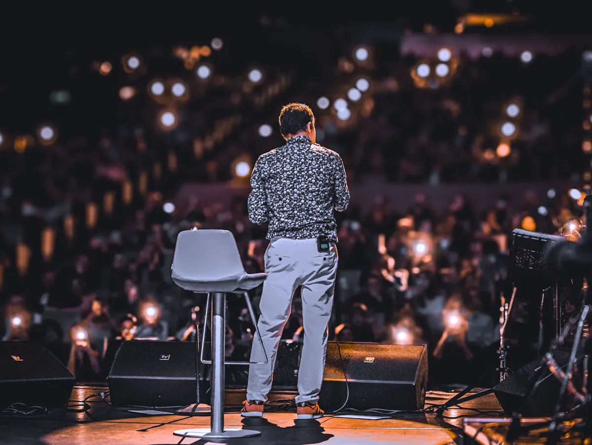 A speaker on a large stage facing an audience holding up lights in the dark