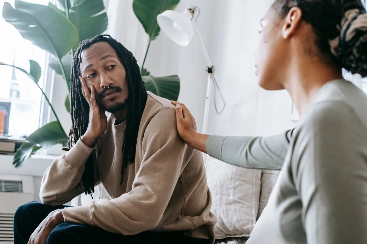 A woman rests a supportive hand on the shoulder of a man working through a hard moment