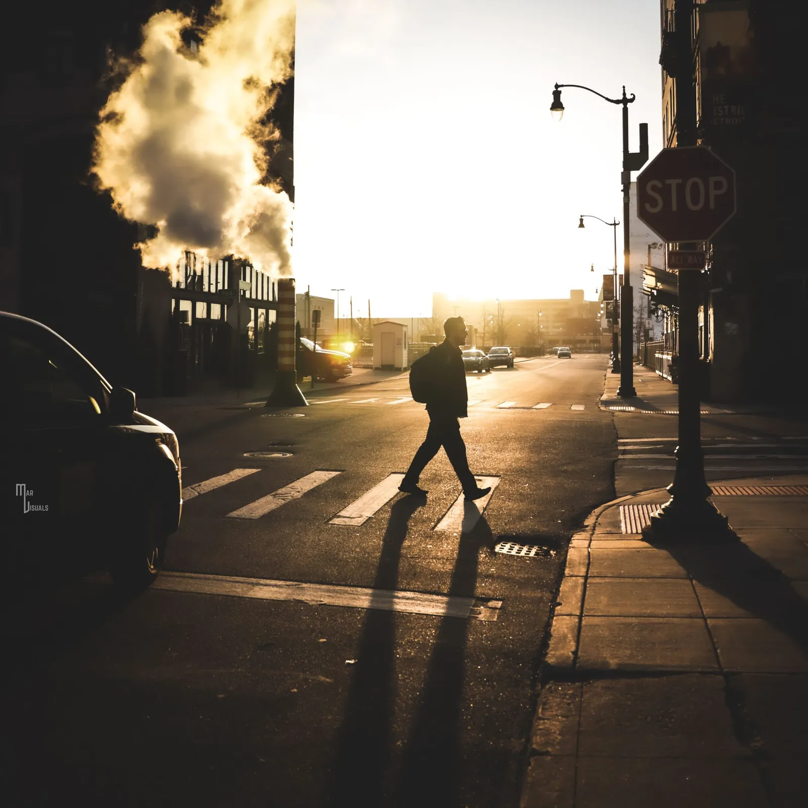 A person crossing a city street in golden early morning light