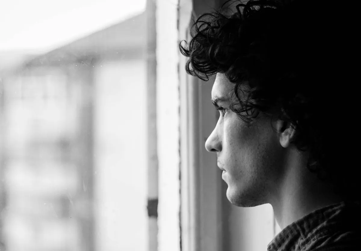 A black and white profile of a young man looking out a window