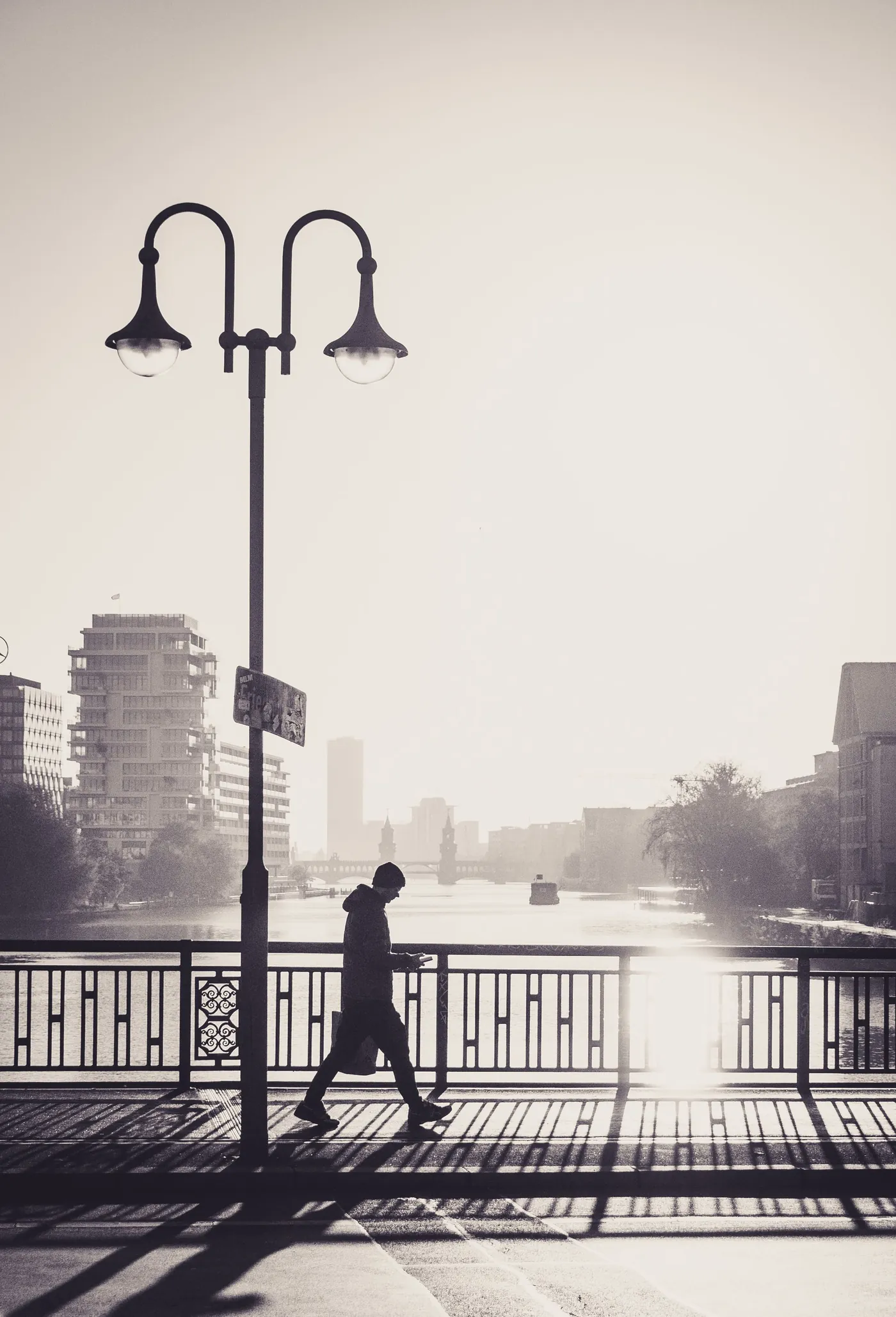 A lone figure walking across a city bridge into pale morning light