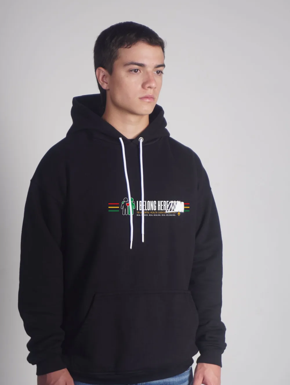 A young man wearing a black hoodie with the I Belong Here TOO chest print