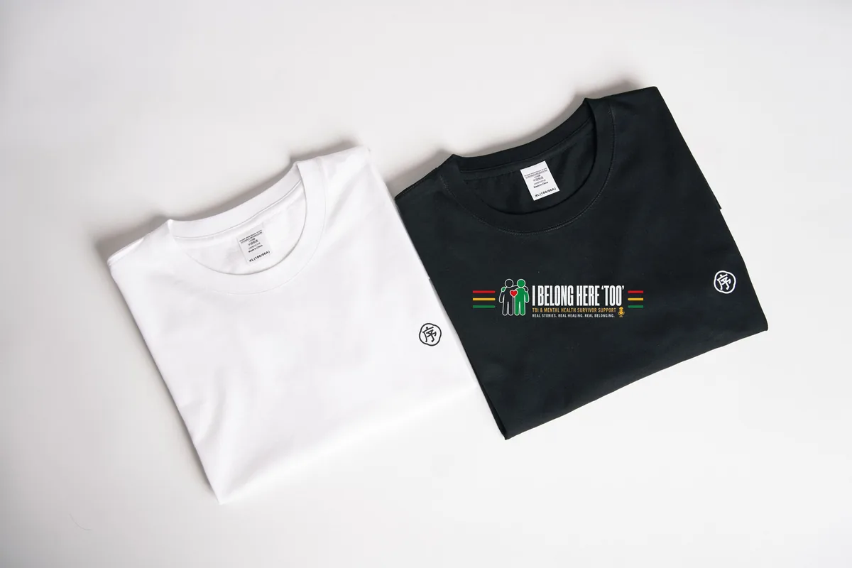 A folded white tee and a folded black tee with the I Belong Here TOO print