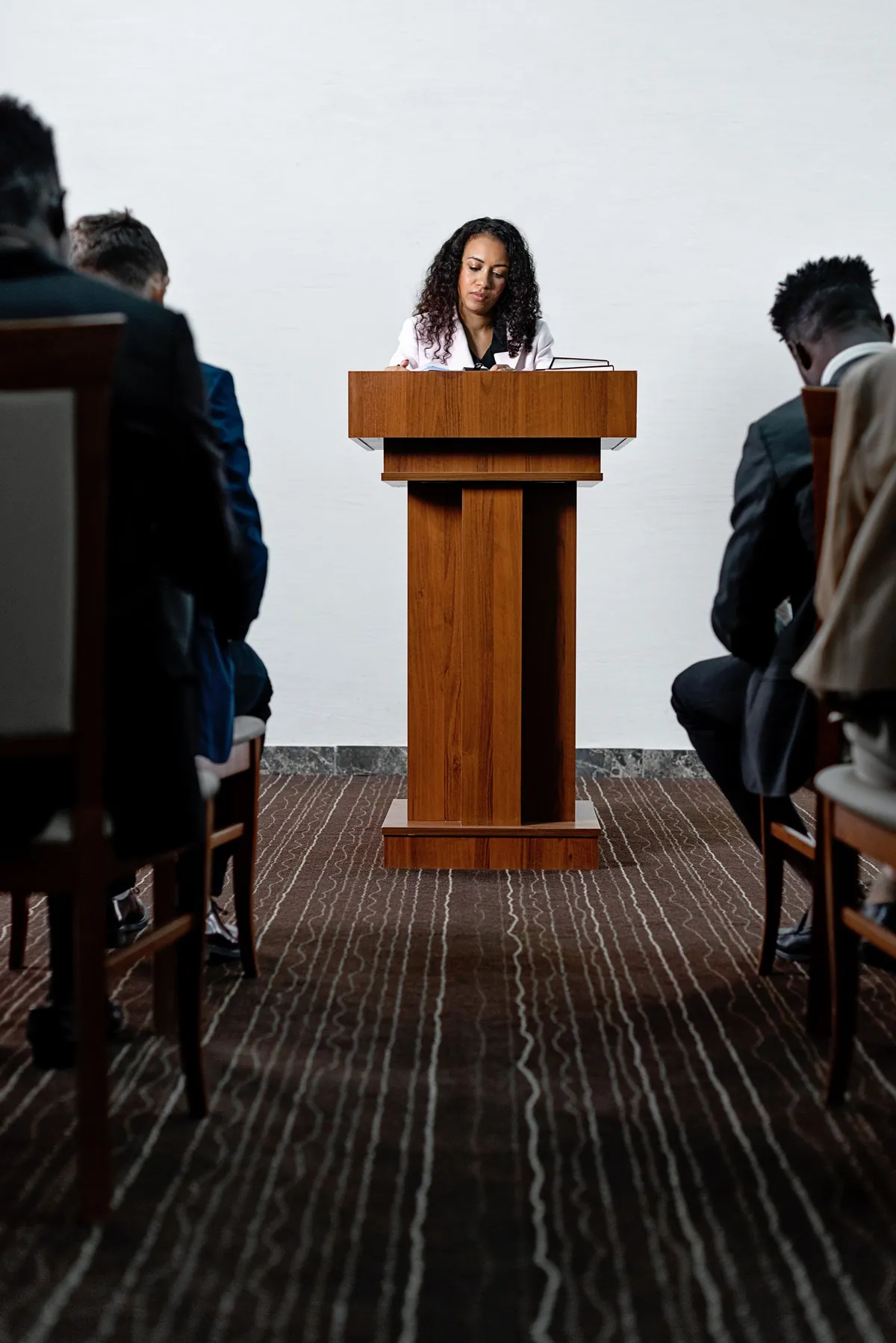 A speaker standing at a wooden podium before a seated audience