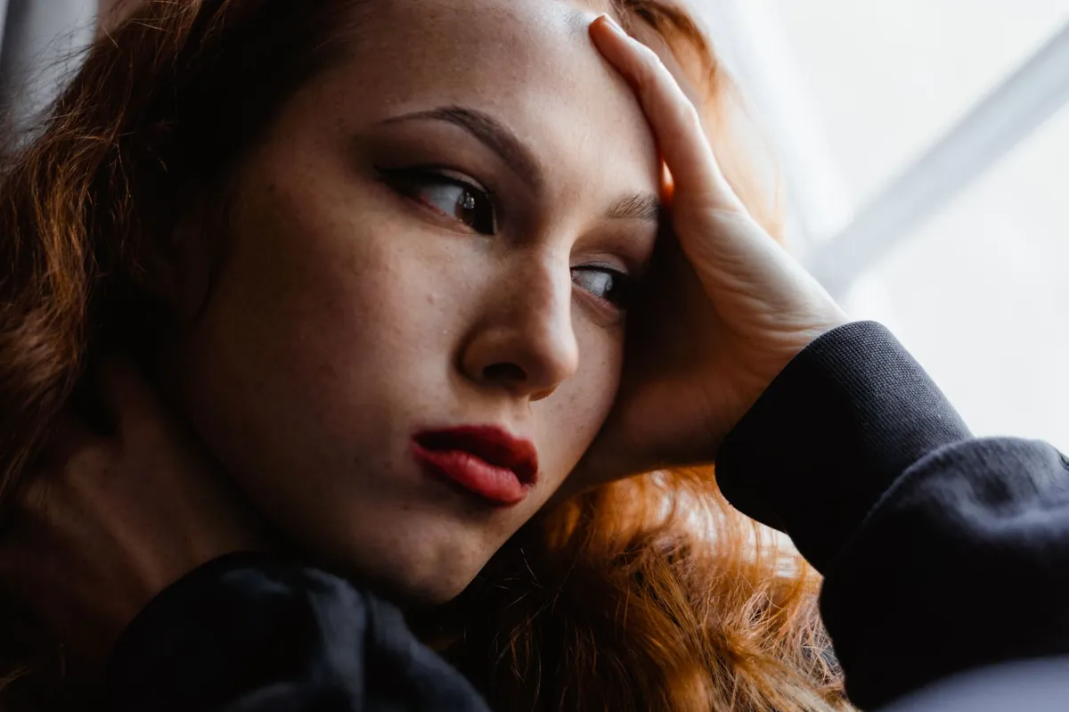 A close portrait of a woman resting her hand against her head, eyes distant