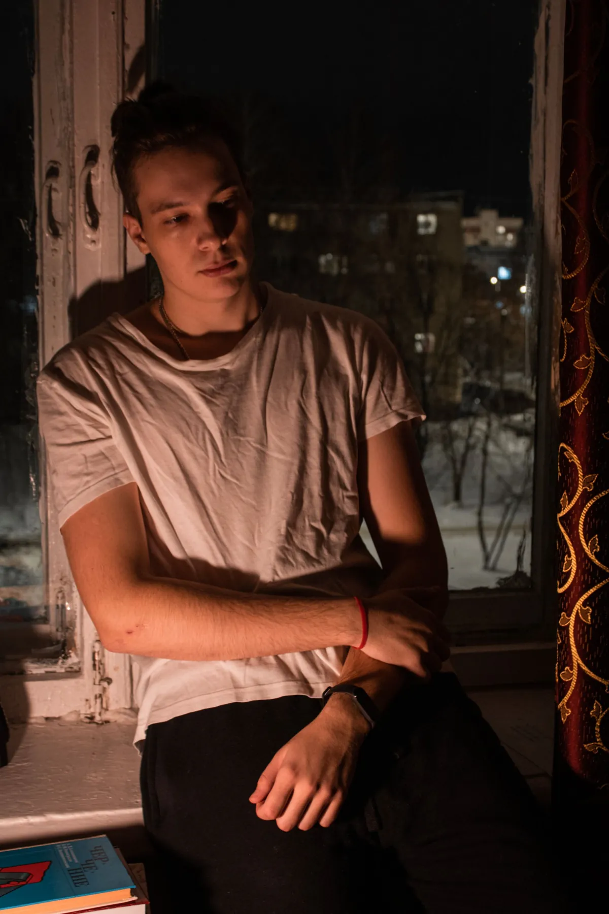 A young man sitting quietly by a window in low evening light