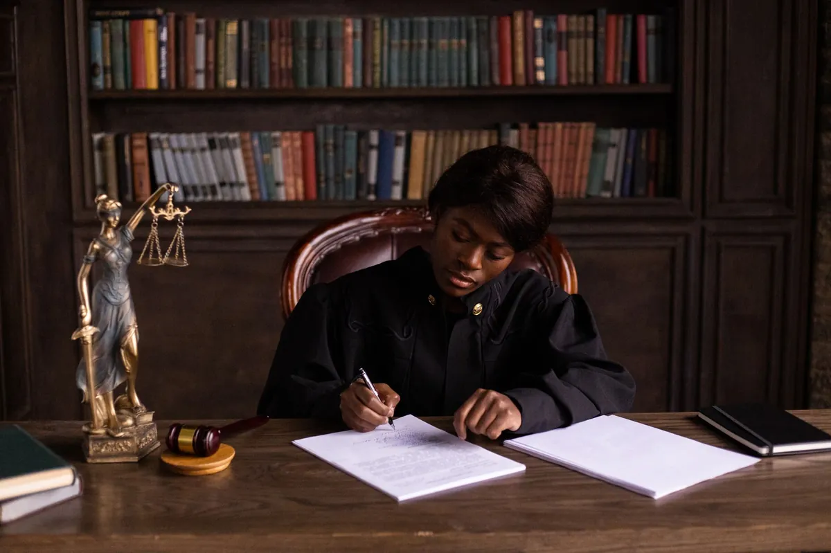 A judge in robes reviewing documents at her desk in a law library