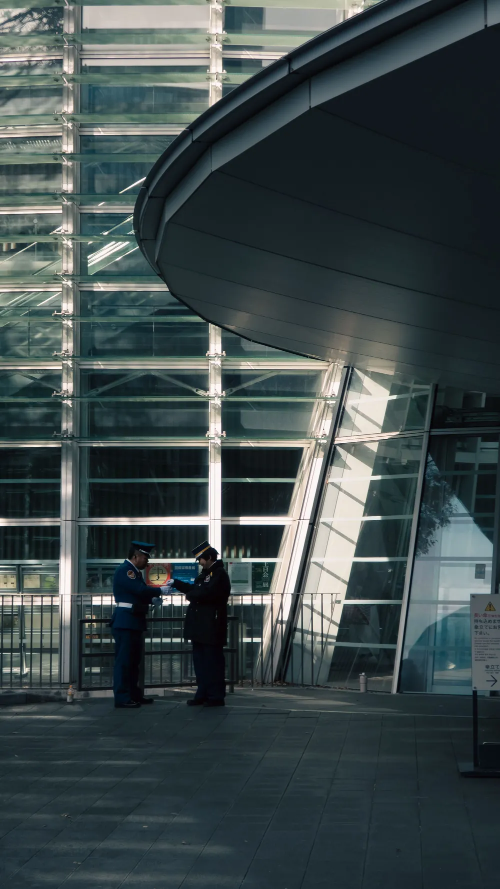 Two security officers reviewing a document outside a modern glass building at dusk